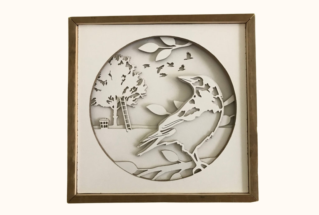 A crow shadowbox cut from layers of hardboard. In the foreground, a crow is perched in the branches. In the background, a flock of crows flies through the sky and a ladder leans up against an apple tree with a basket of apples at the bottom. 