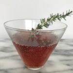 a cocktail glass of pomegranate spritzer with a rosemary sprig garnish