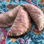 three cherry turnovers with pink icing arrayed on top of a blue floral cloth